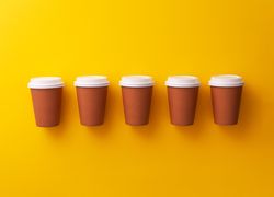 Single row of disposable coffee cups on yellow background