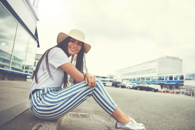 Woman sitting calmly on curb smiling wearing striped trousers and silver shoes