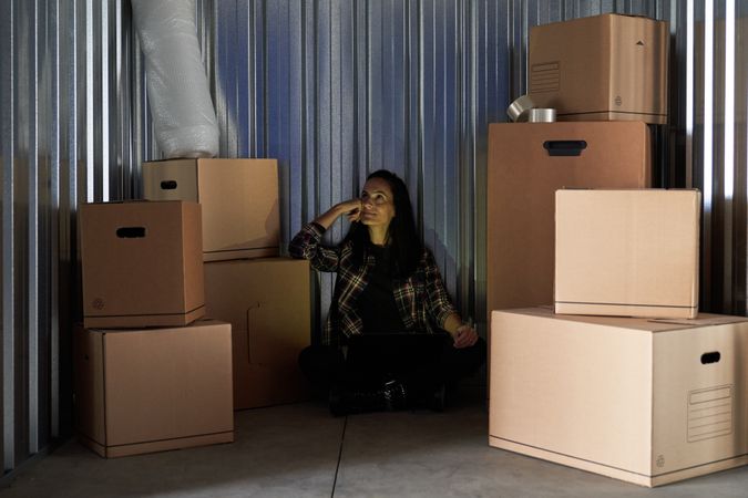 Young woman inside a warehouse to store moving boxes organizing with her laptop