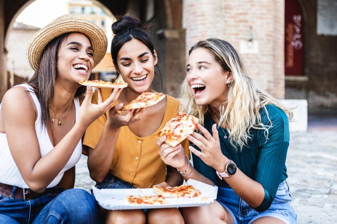 Three very happy female friends eating pizza on Italian street