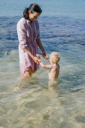 Woman and small kid having fun with water while relaxing on seacoast at resort