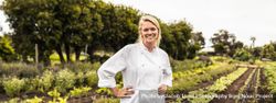 Cheerful chef smiling at the camera with her hands on her hips standing on a farm 5kdn64