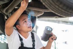 Male auto repairman looks up at undercarriage of vehicle