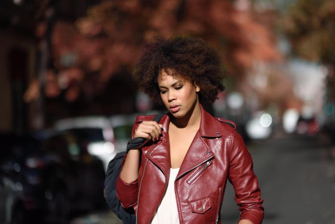 Woman looking down in red leather jacket standing in sunny road