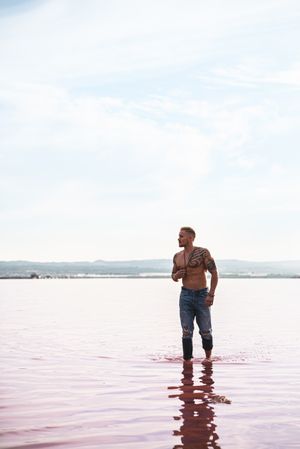 Undressed muscular man walking on shore of pink lake
