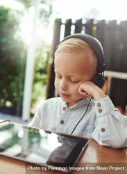 Blond boy using headphones and watching show on digital tablet, vertical 0VkXO5