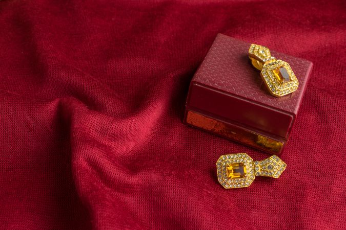 Beautiful shiny golden earrings with diamond studded Indian traditional design on a red velvet background