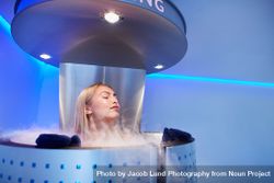 Woman in cryotherapy chamber with steam coming out over the top 0gXAJ7