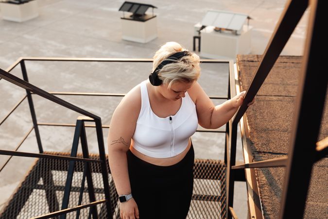 Curvy blond woman in headphones walking up the stairs