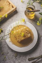 Whole raw honeycomb on table with honey jar and wooden dipper, yellow flowers with petals