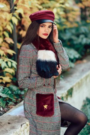 Female fixing hair in warm clothes perched on wall with orange leaves