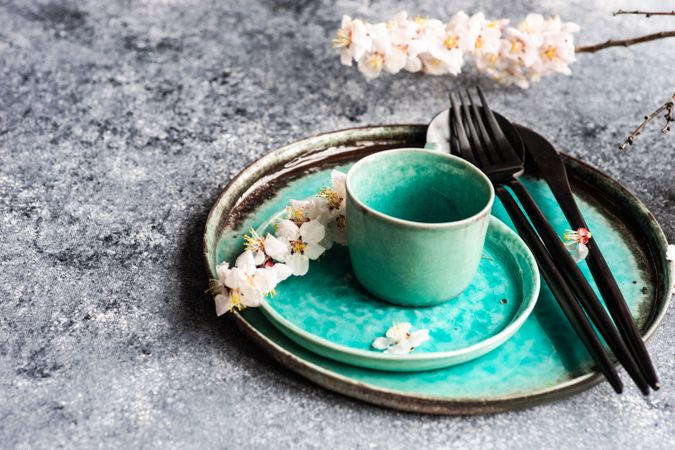 Spring floral concept with top view of apricot blossom branch on teal plates on grey table