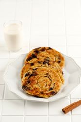 Round plate of sweet raisin cinnamon roti parata or roti canai with milk, vertical