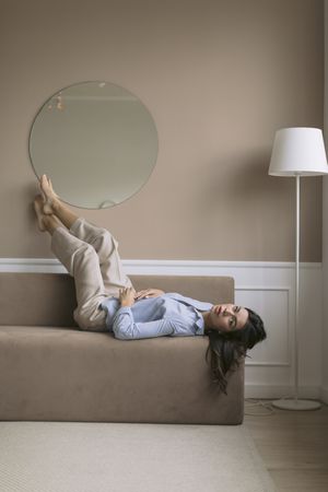 Woman lying on a couch with her feet resting on the wall above her