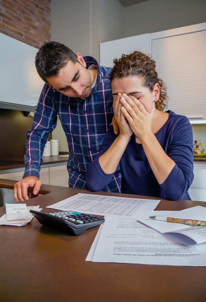 Sad couple going through their bills together in the kitchen, vertical