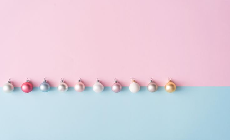 Row of colorful Christmas baubles on blue and pink pastel background