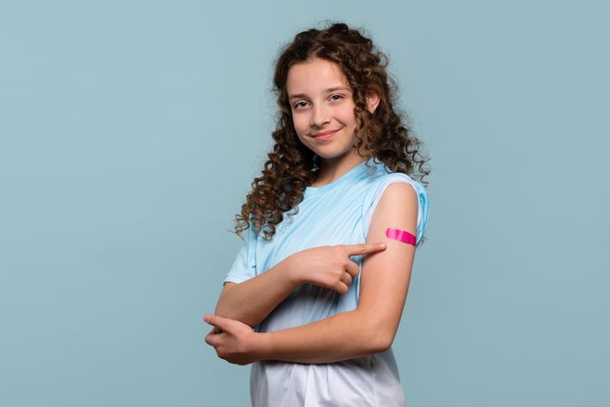Girl pointing at vaccinated arm with pink bandage.