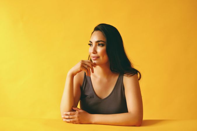 Hispanic woman looking away and thinking while sitting in yellow room, copy space
