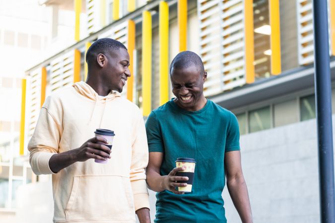Happy best Black friends laughing with takeaway coffee on street