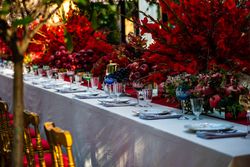 Elegant formal dinner table with glass ware, bowls of fruit and large red floral arrangements