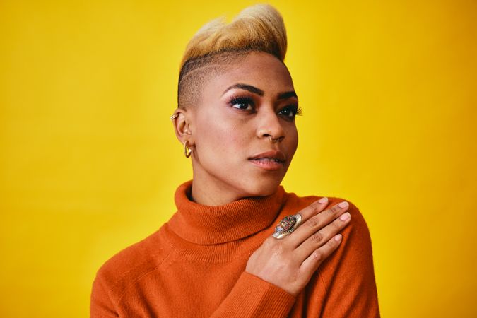 Studio shot of confident Black woman posing with short blonde hair in orange sweater