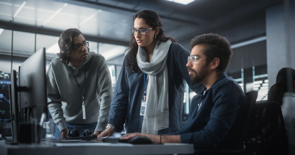 Team of Three Multiethnic Diverse Software Developers Talk, Discuss an AI Project.