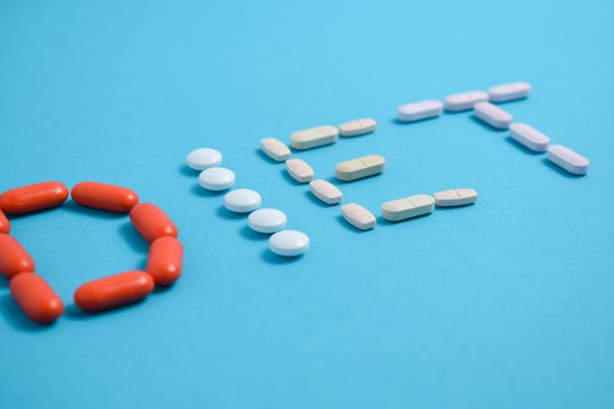 Various pills spelling the word "DIET" on blue background