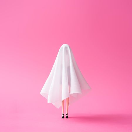 Doll under ghost sheet costume against pastel pink background