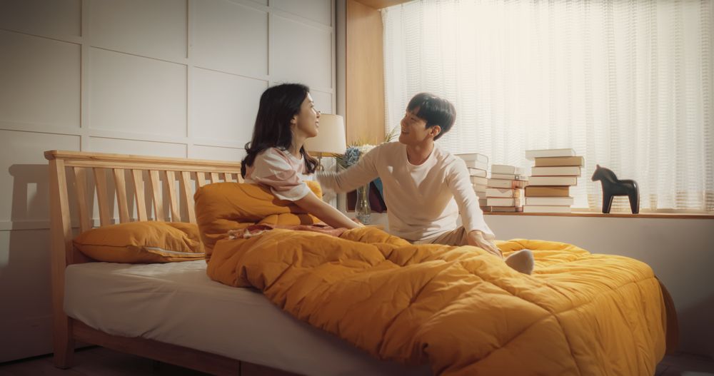 Young Korean Couple Sleeping in Bed, Sun Shines on Them, They Look at Each Other and Greet New Sunny Day.