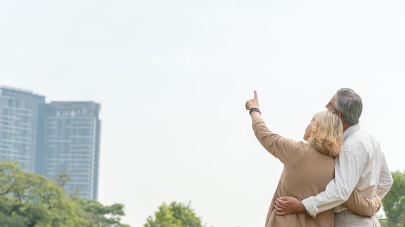 Banner shot of mature man and woman standing in park and pointing up