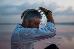 Man with fish tank on head sitting at seashore