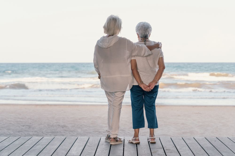 older women hugging each other and looking at sea on beach