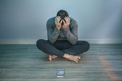 Man with problems sitting on the floor behind of his mobile