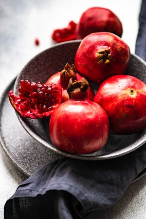 Dark bowl full of fresh whole pomegranates, vertical composition