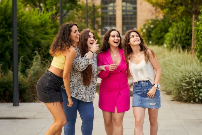 four smiling friends pointing upward and looking in that directi