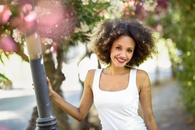 Young Black woman with afro hairstyle smiling in park with sun flare