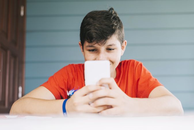 Teenage male wearing red t-shirt sitting outdoors using phone