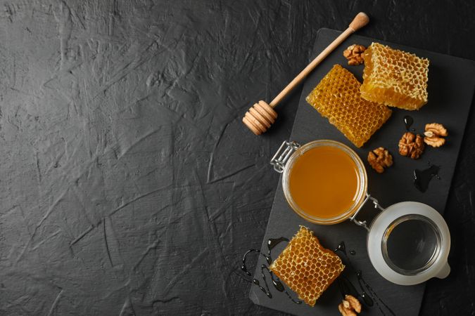 Walnut, honeycombs, jar with honey and dipper on dark background, copy space