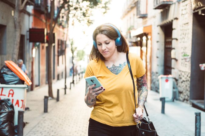 Inspired woman in headphones listening to music on smartphone on street