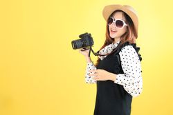 Happy Smiling Young Asian Woman Tourist in Summer Hat and Sun Glasses Standing with Camera