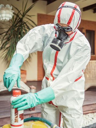 Man in suit for fumigation pouring chemical into tank