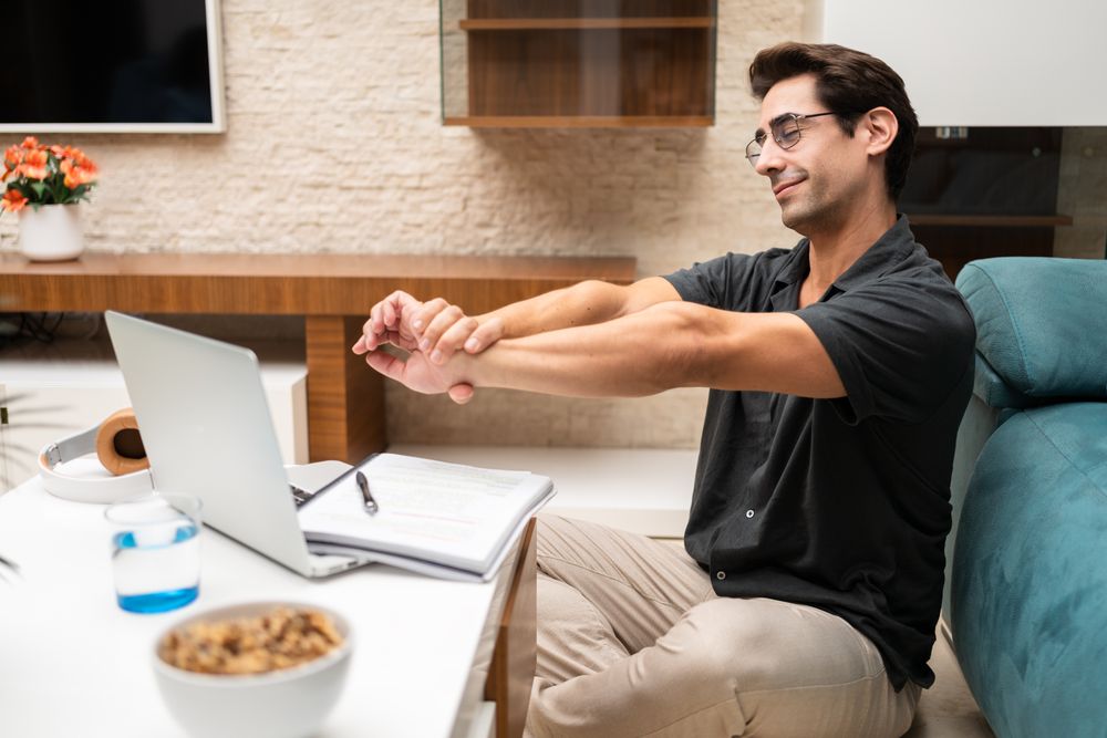 Man stretching while working from home with laptop and notepad