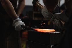 Blacksmiths forging hot metal with hammer in workshop