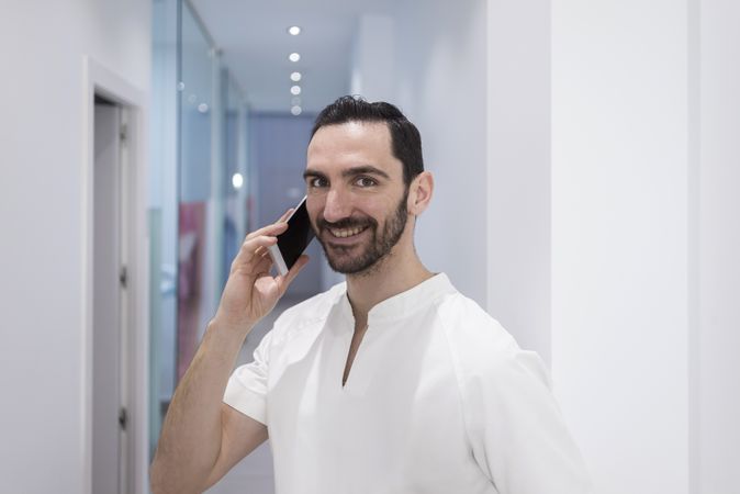 Smiling bearded medical professional talking using a smartphone at hospital