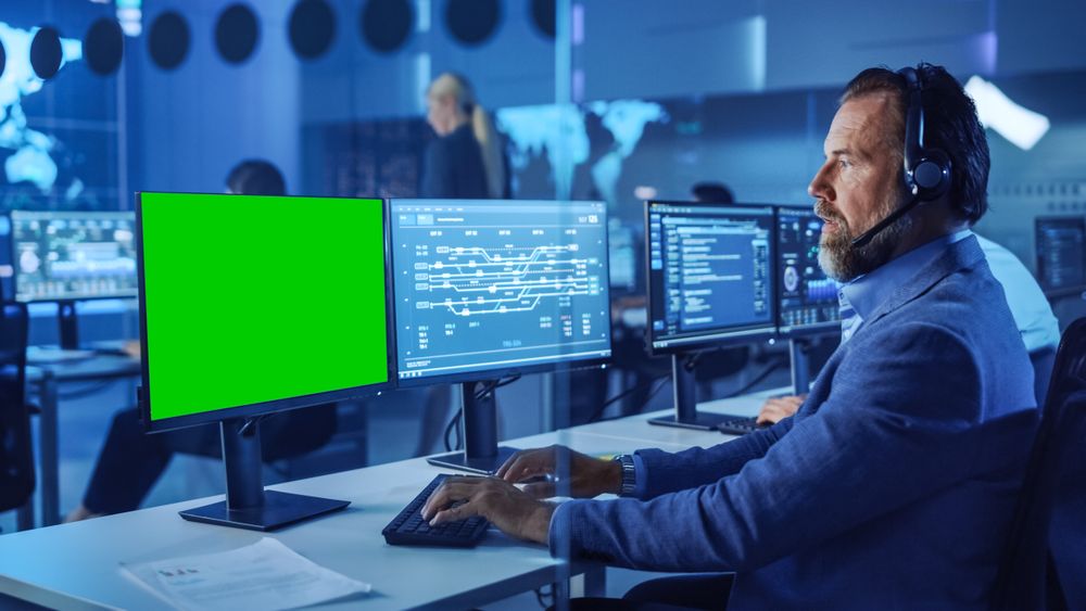 Bearded Technician Monitors Data on Multiple Screens in Futuristic Blue-lit Control Room.