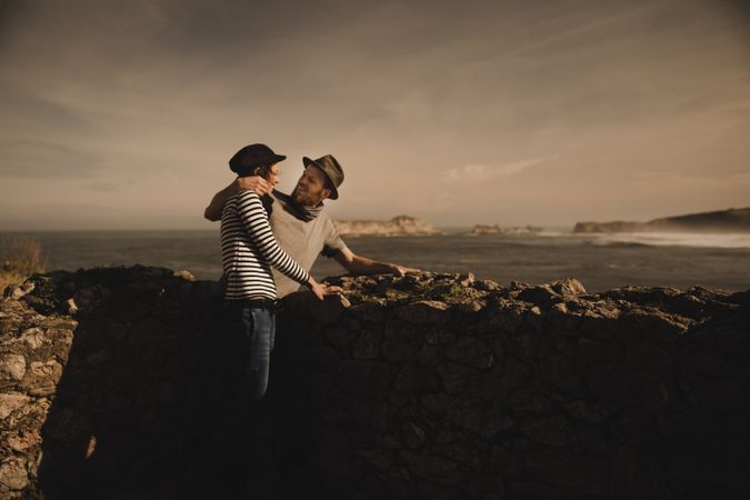 Man holding woman on hands near stones on shore