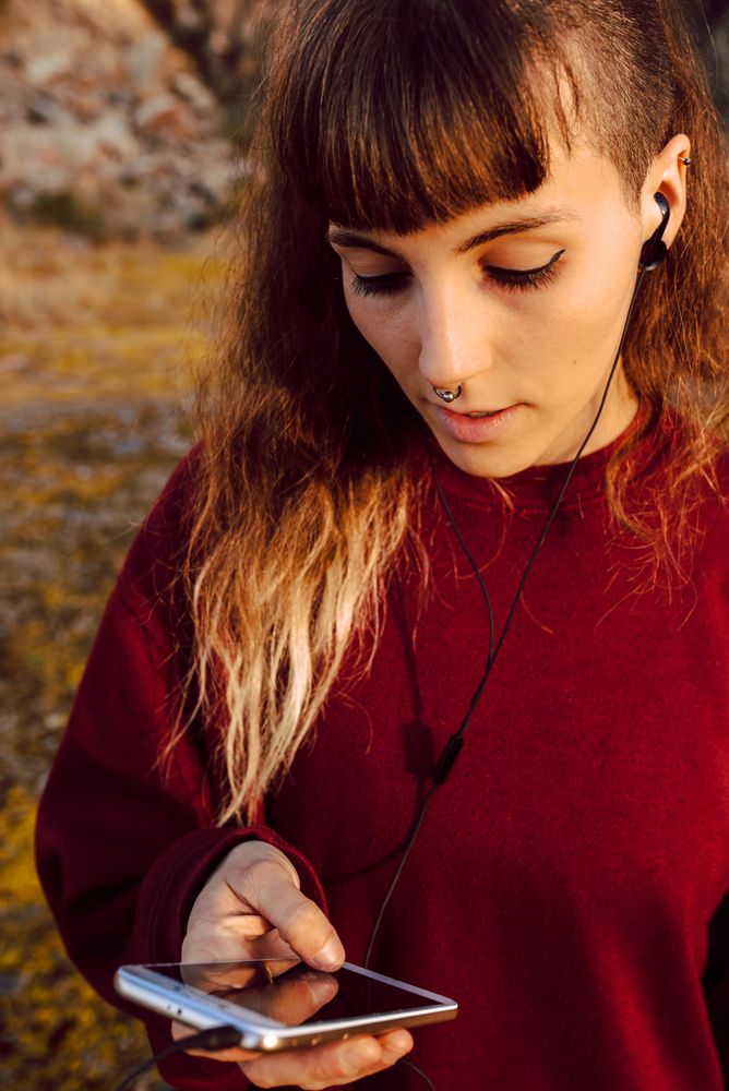 Young woman with piercing listening music on smartphone on hill
