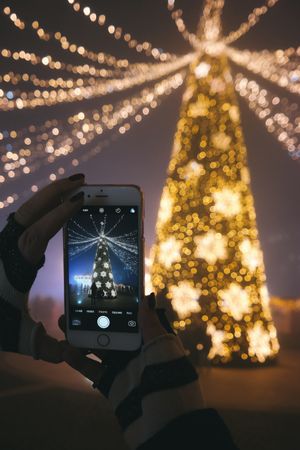 Cropped image of person taking photo of yellow lit Christmas tree with smartphone