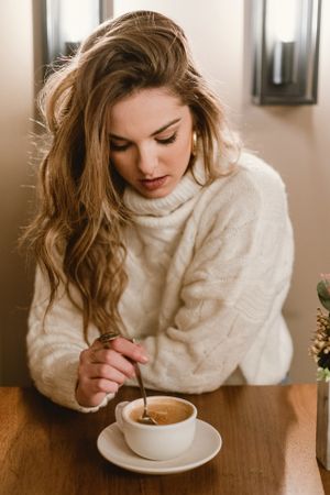 Elegant woman mixing coffee in cafe