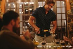 Man serving champagne to friends at dinner party 56vZd5